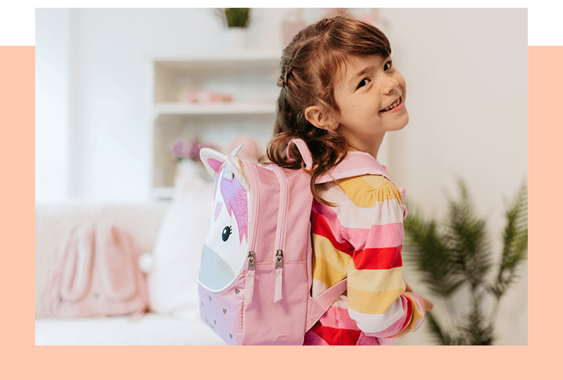Lächelndes Kindergartenkind mit Einhorn-Rucksack im Kinderzimmer