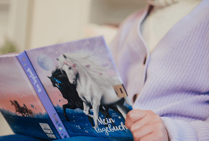 Miss Melody Tagebuch in Hand eines Mädchens mit lila Strickjacke