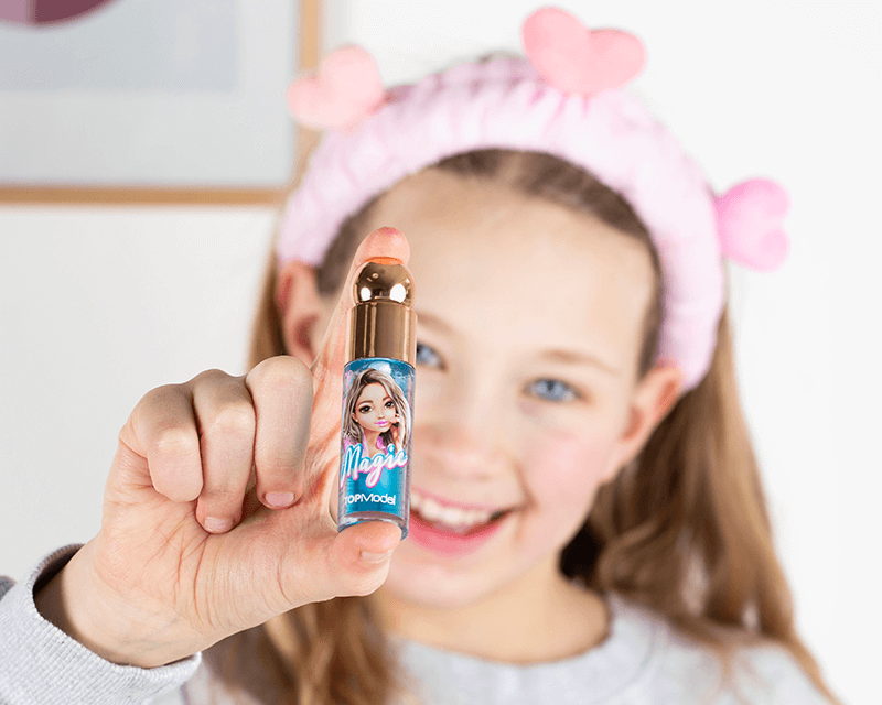 Mädchen mit TOPModel Haarband hält Lipgloss für Kinder ins Bild